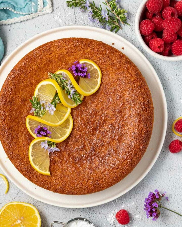 vegan almond cake on a plate topped with swirly lemon slices and purple flowers