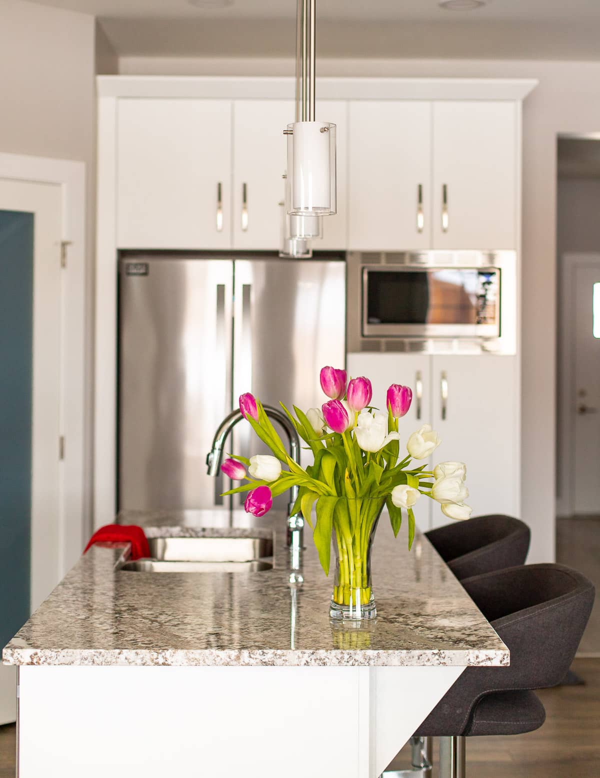 A white kitchen with a vase of tulips on the counter. 