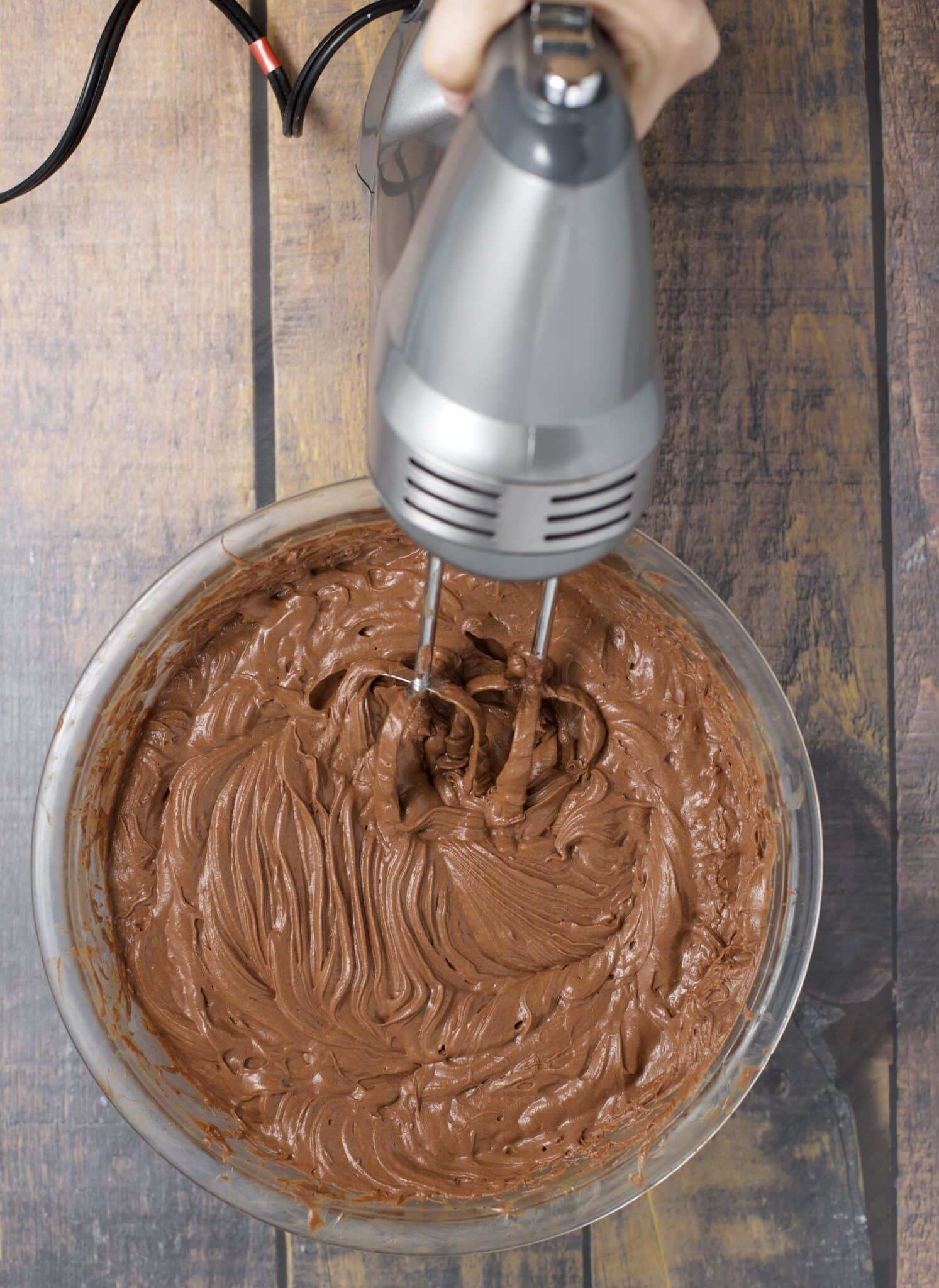 an electric hand mixer blending a chocolatey mixture in a bowl 