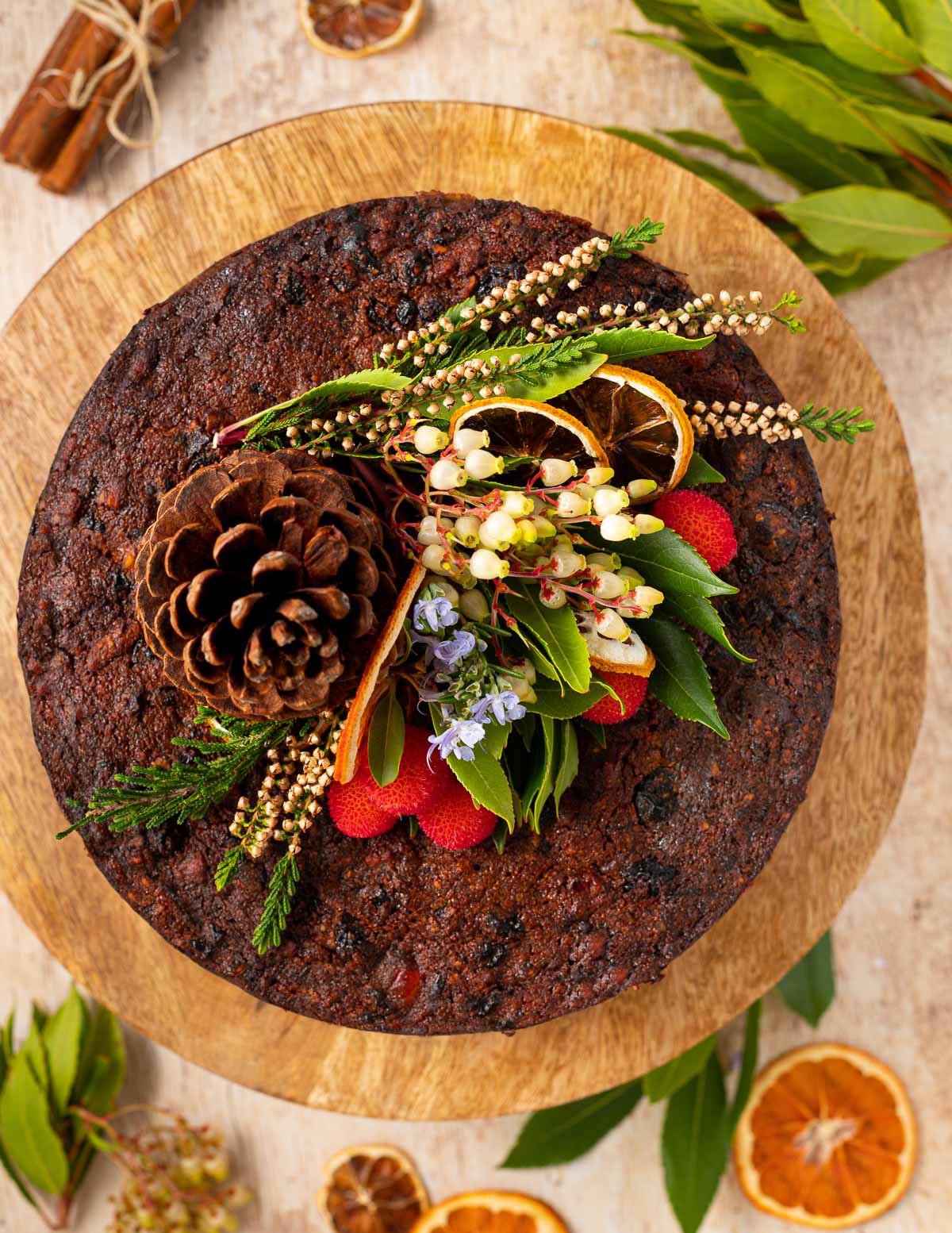 a plain vegan Christmas cake decorated with a pine cone, leaves and flowers