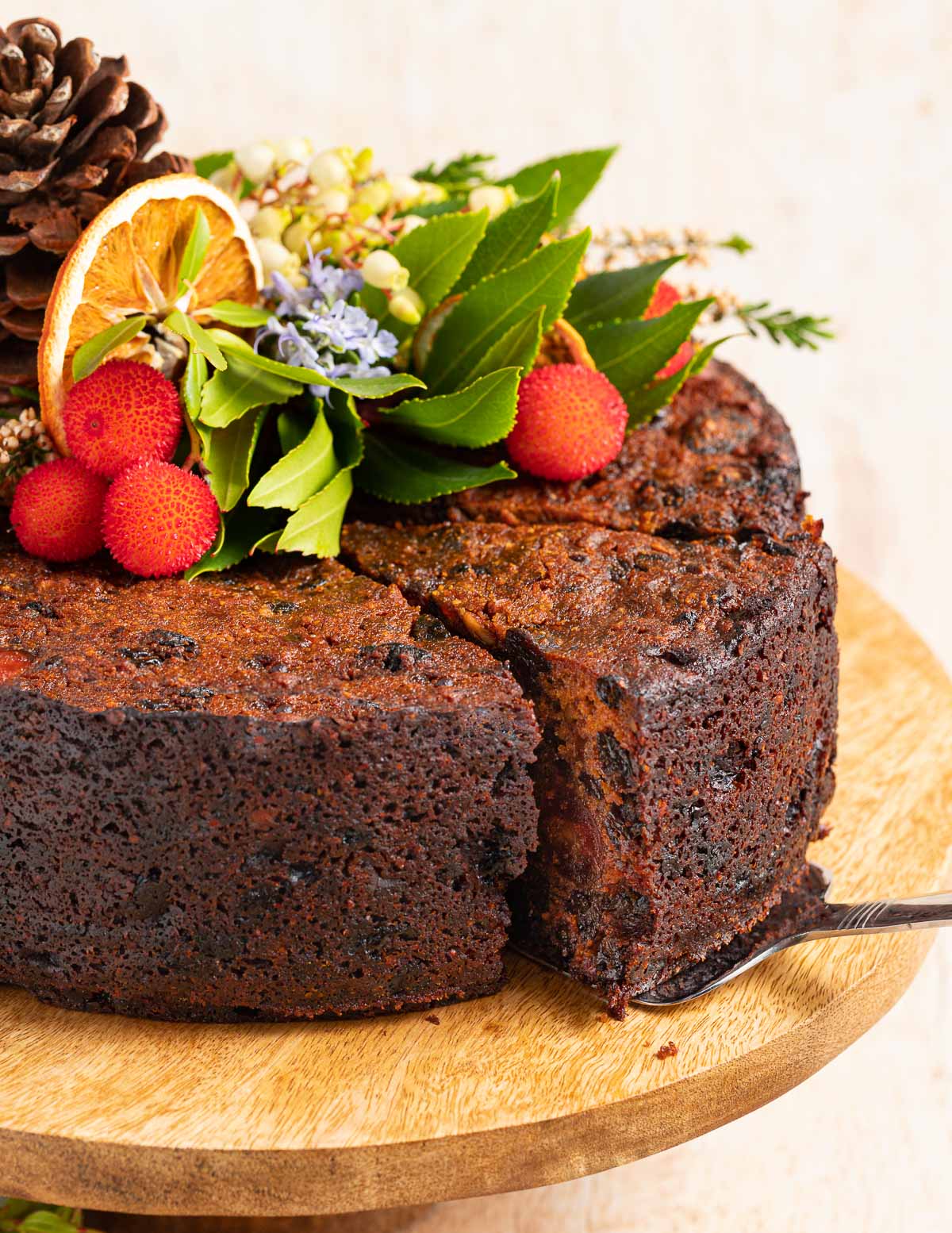 vegan fruit cake decorated with greenery, dried orange slices, fruit from a strawberry tree and a pine cone