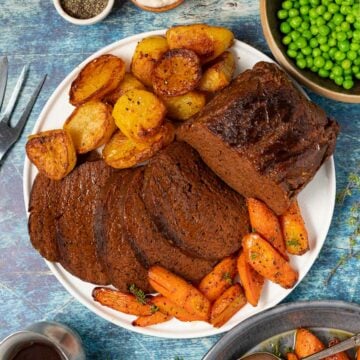 sliced vegan beef surrounded by roast potatoes and carrots