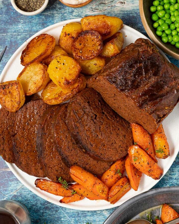 sliced vegan beef surrounded by roast potatoes and carrots