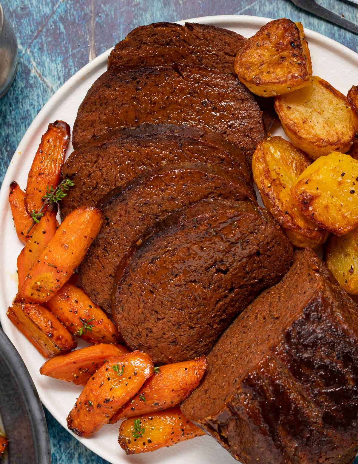 sliced vegan beef roast surrounded by roast potatoes and carrots
