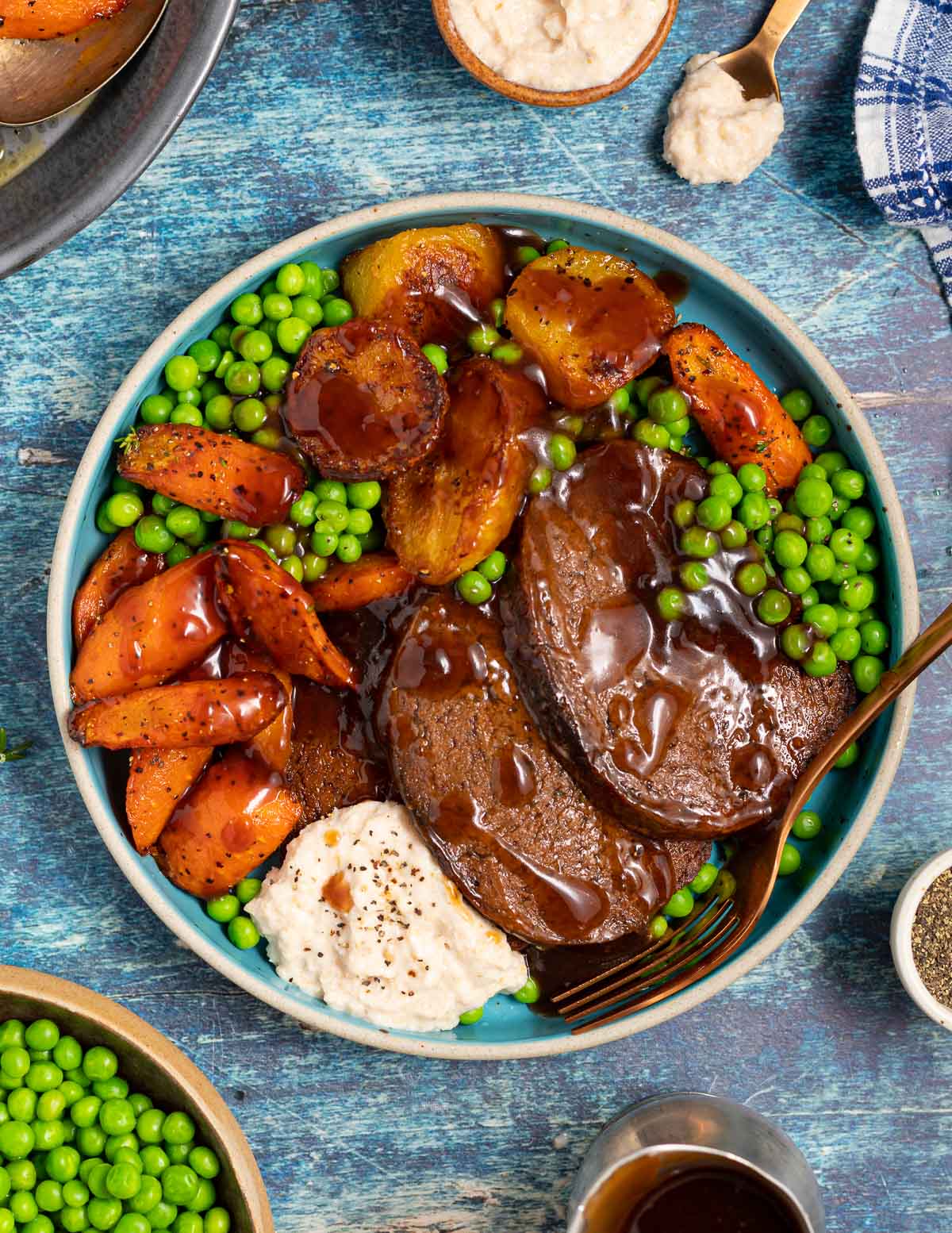 a dinner plate with vegan beef, roast potatoes, carrots, peas and horseradish sauce