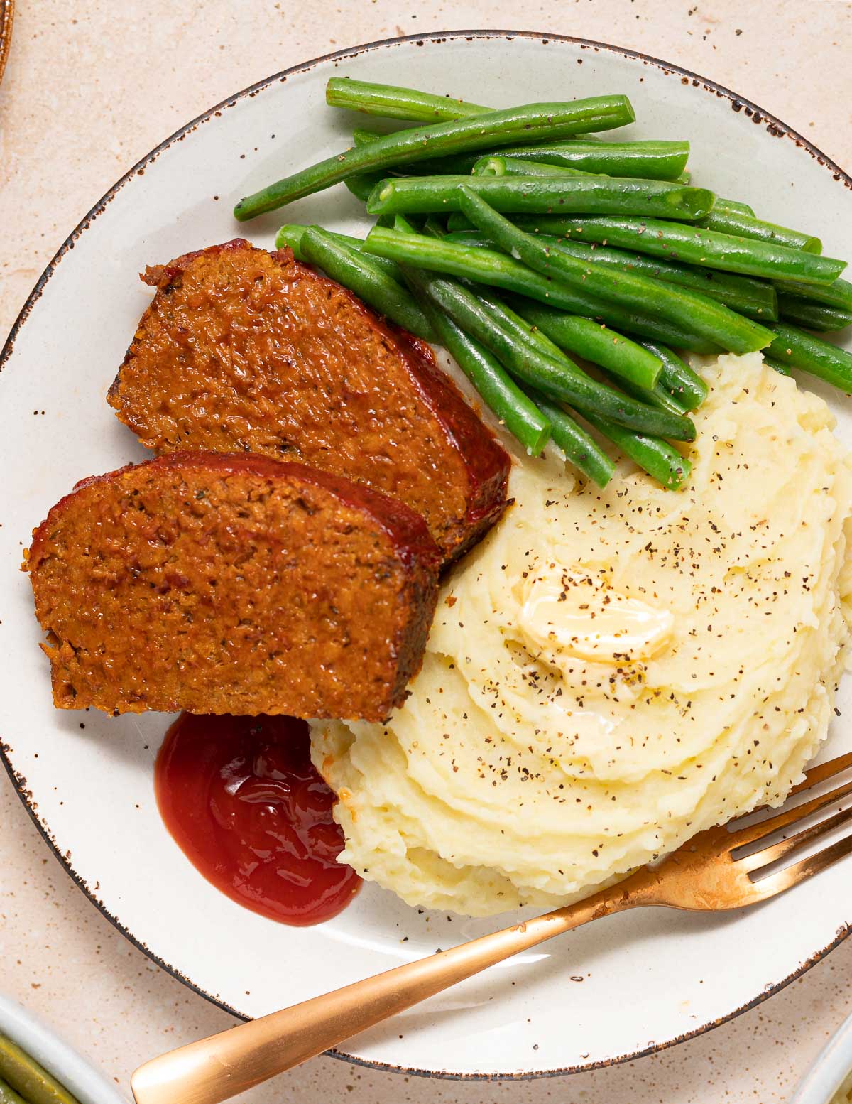 2 slices of meatloaf on a plate with mashed potato and green beans