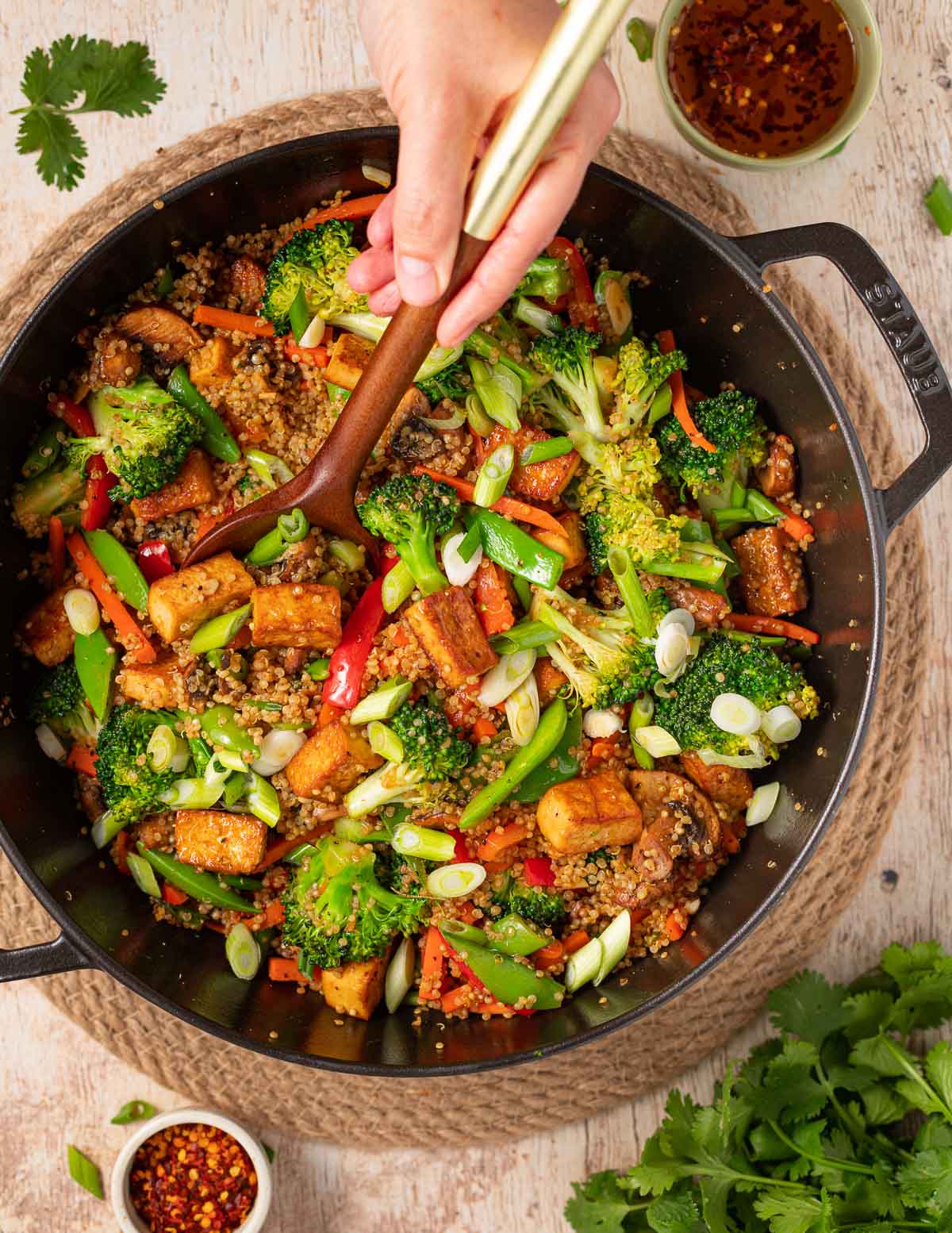 a handheld wooden spoon in a large pan of tofu quinoa stir fry