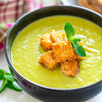 a bowl of green pea soup with croutons in a black bowl