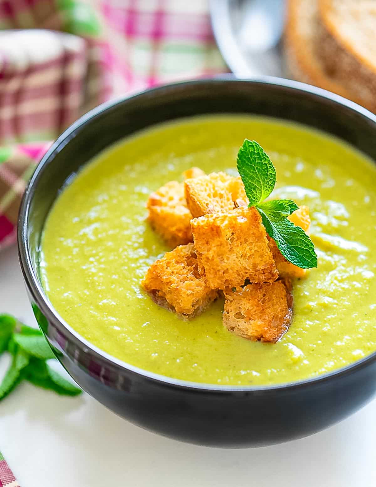 a bowl of vegan pea soup with croutons and a sprig of fresh mint 