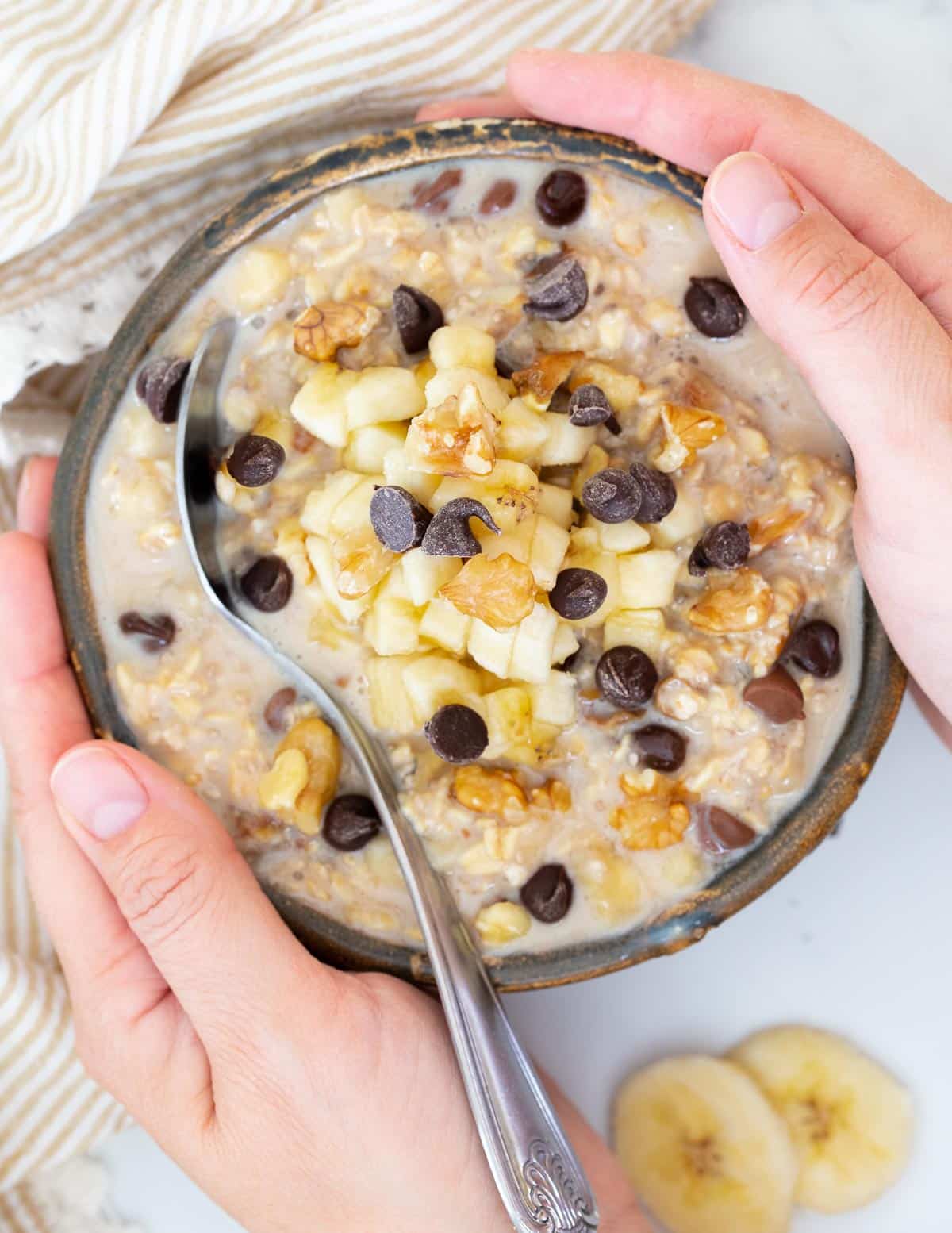 a bowl of chunky monkey overnight oats with hands around it