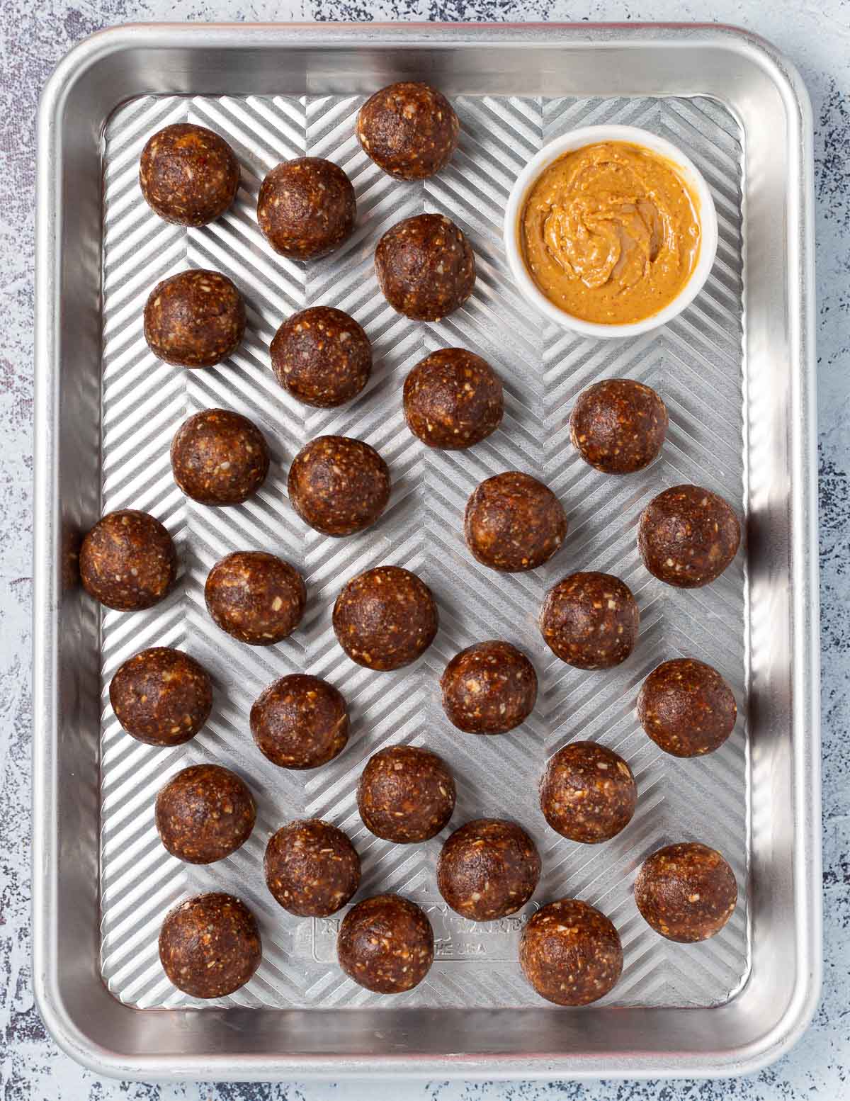 protein balls on a baking tray with a bowl of peanut butter