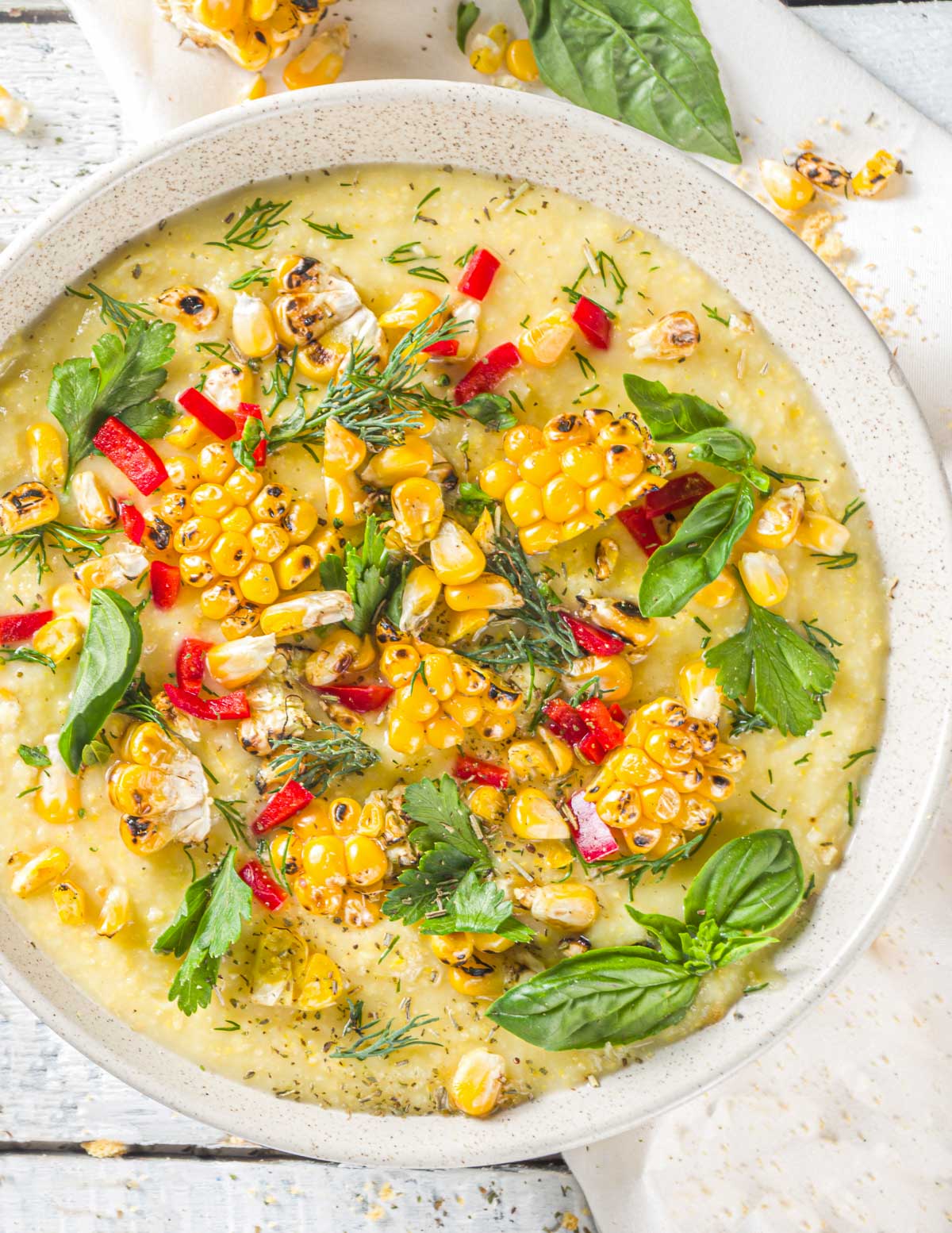 a bowl of vegan corn chowder topped with grilled corn pieces, fresh herbs and chopped red bell pepper