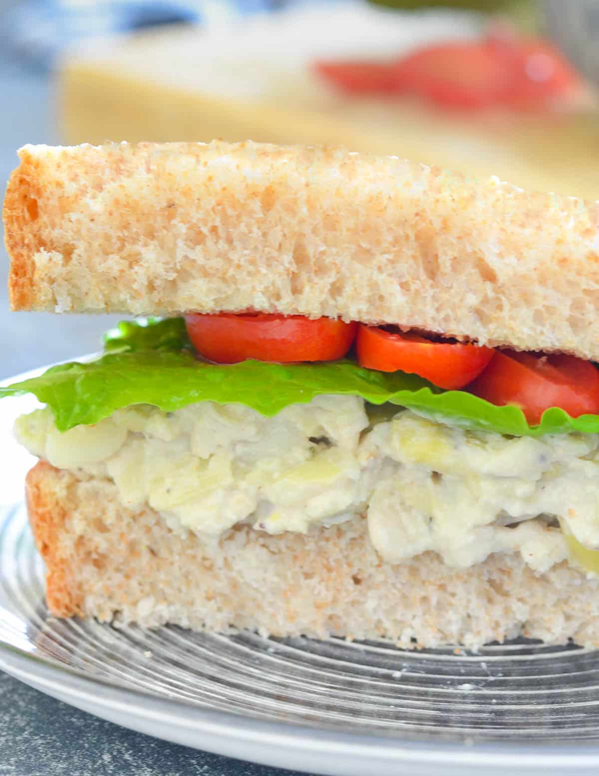 close up of a sandwich with creamy white bean and artichoke filling, lettuce and tomato