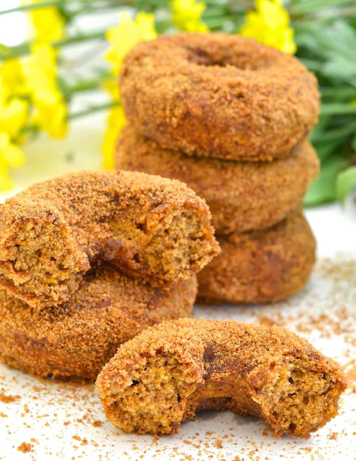 stacked vegan pumpkin donuts with one cut in half so you can see the fluffy insides