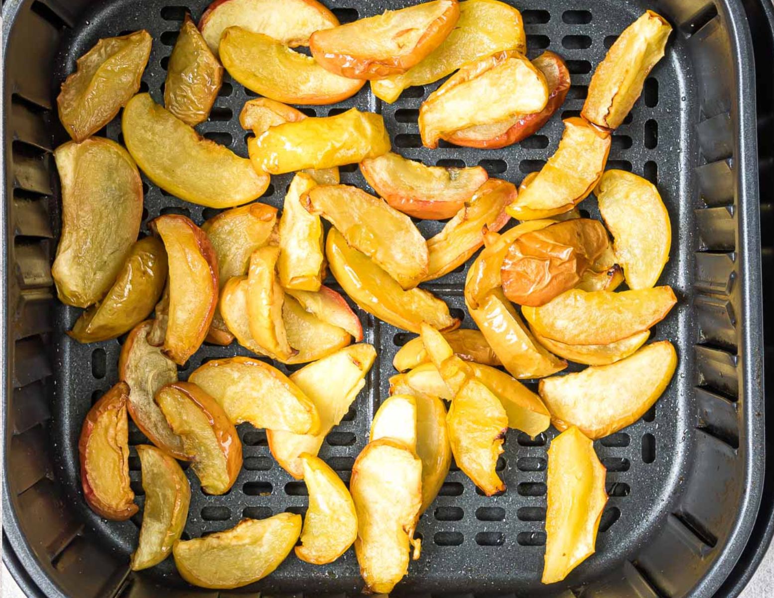 cooked apple slices in an air fryer basket