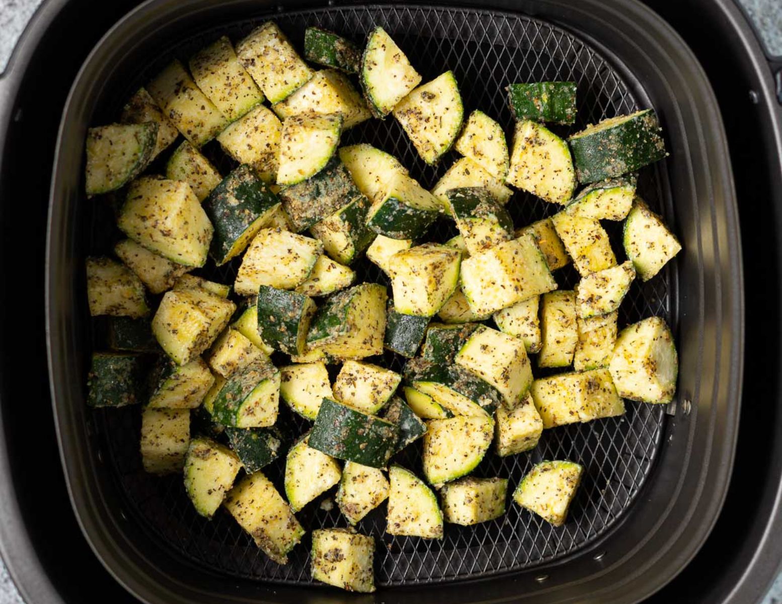 uncooked seasoned zucchini in an air fryer basket