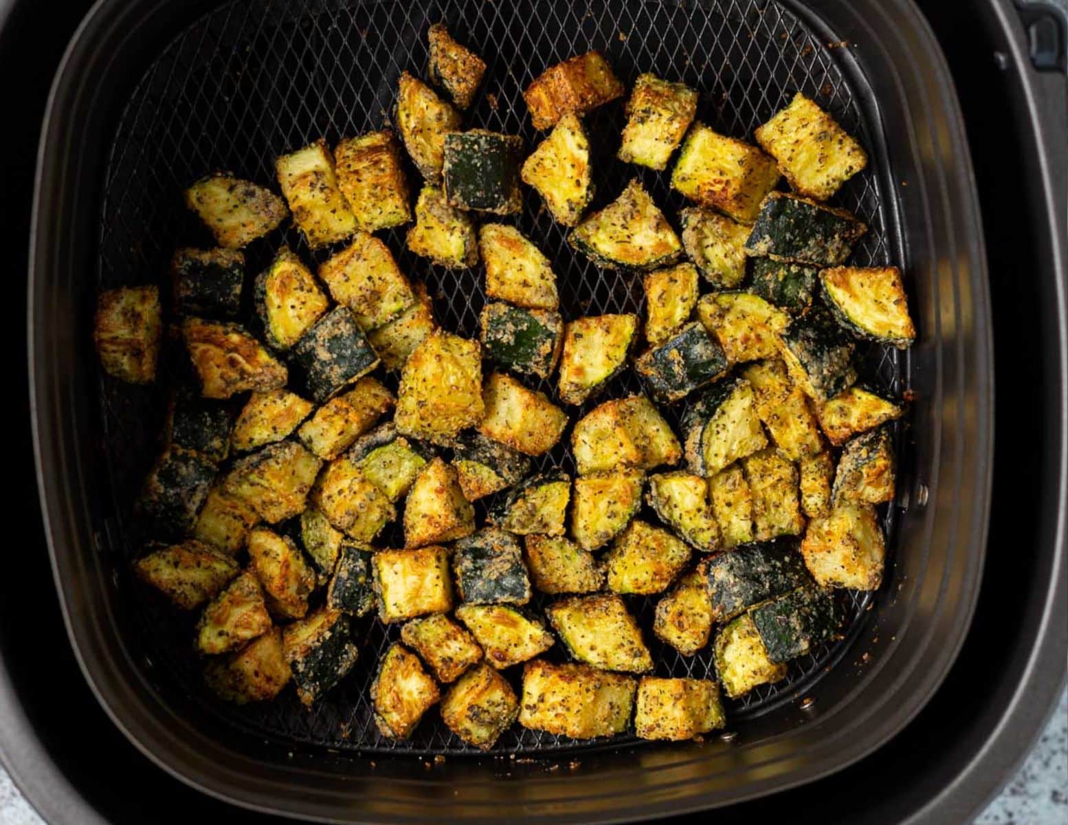 golden crispy zucchini pieces in an air fryer basket