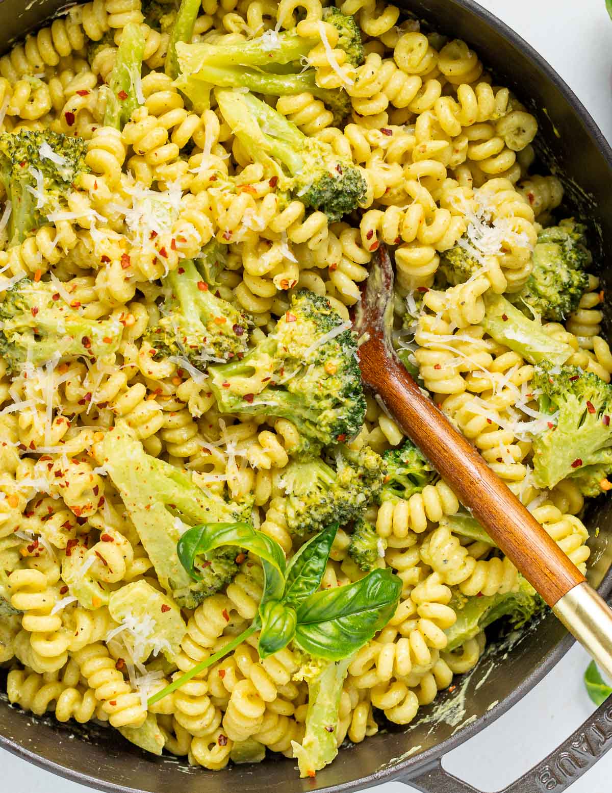 a skillet of vegan broccoli pasta garnished with vegan parmesan and fresh basil