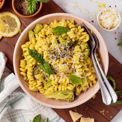 a pink bowl of broccoli pasta with a fork and spoon