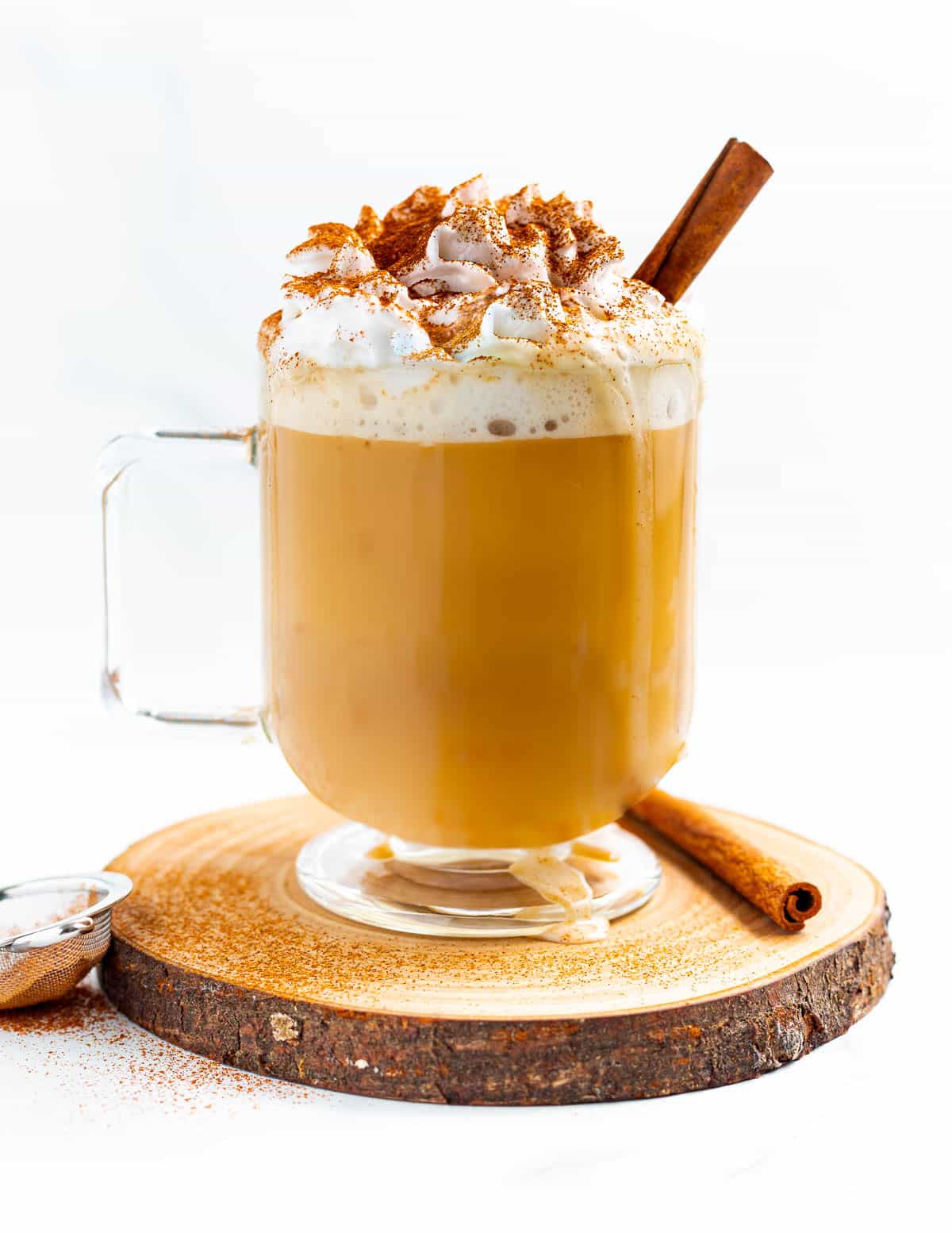 a glass latte mug full of creamy pumpkin spice latte and topped with dairy-free whipped cream and a stick of cinnamon. 