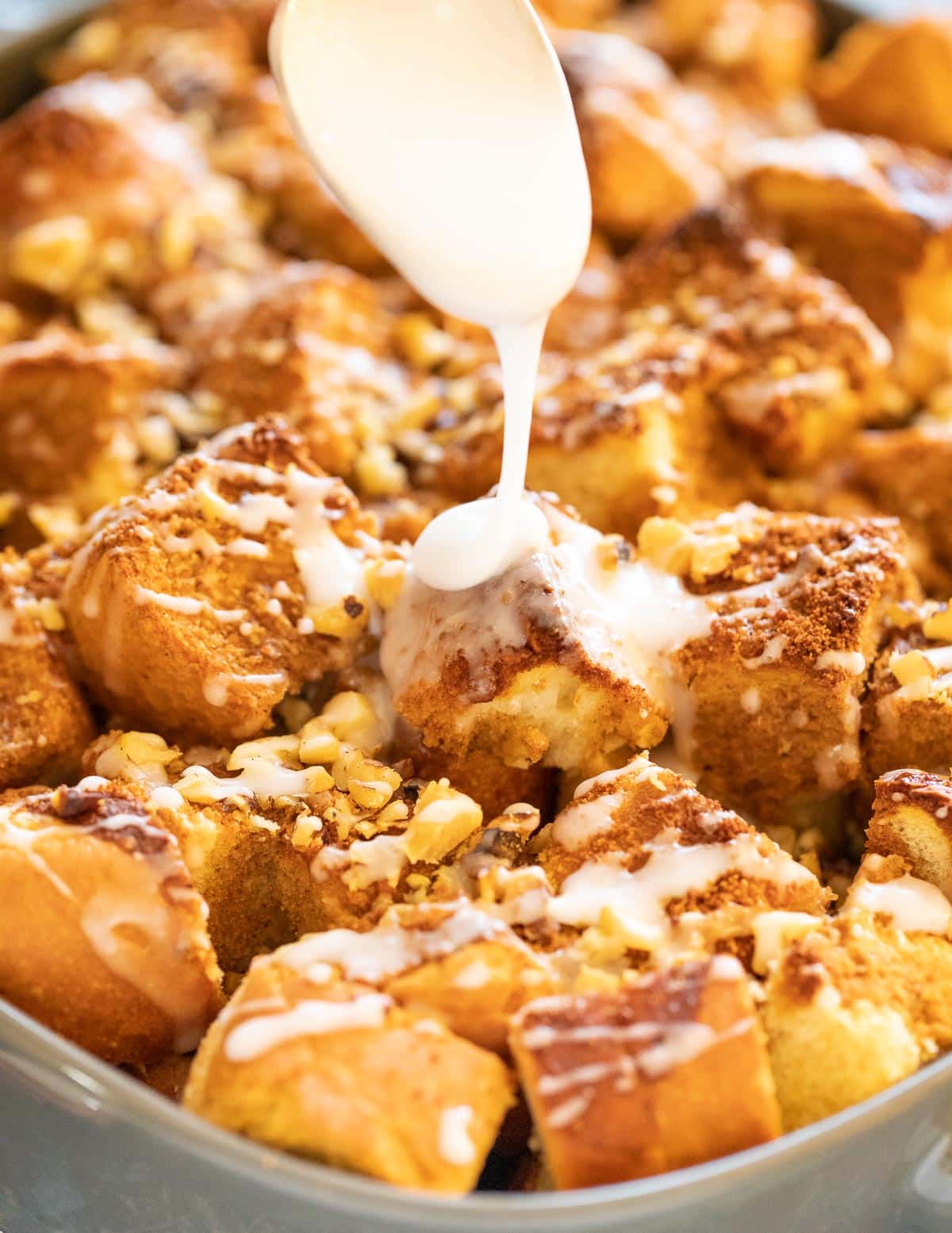 a close up picture of the crusty, golden cubes of bread on top of the vegan French Toast casserole while being drizzled in icing. 