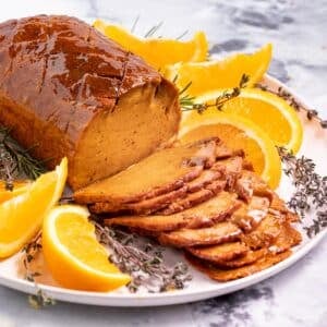 a sliced vegan ham surrounded by orange wedges and herbs