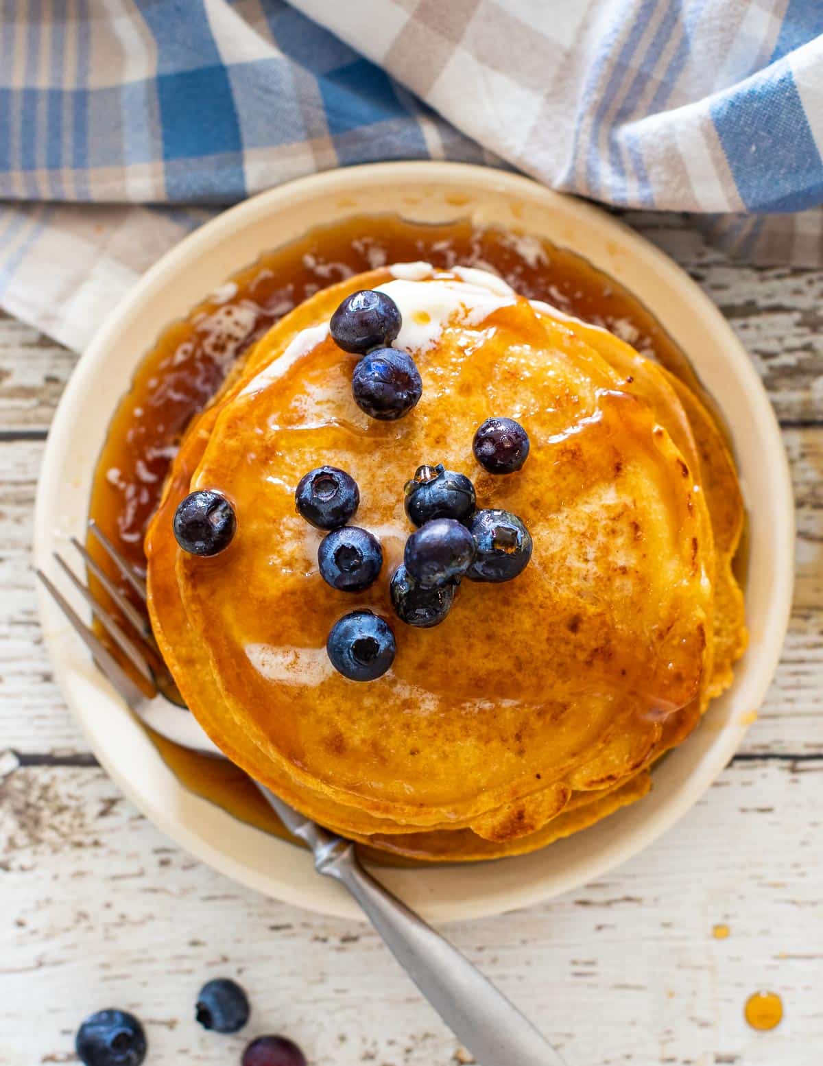 a stack of corn flour pancakes topped with blueberries and lots of syrup