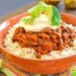 a bowl of chili topped with sour cream and lime