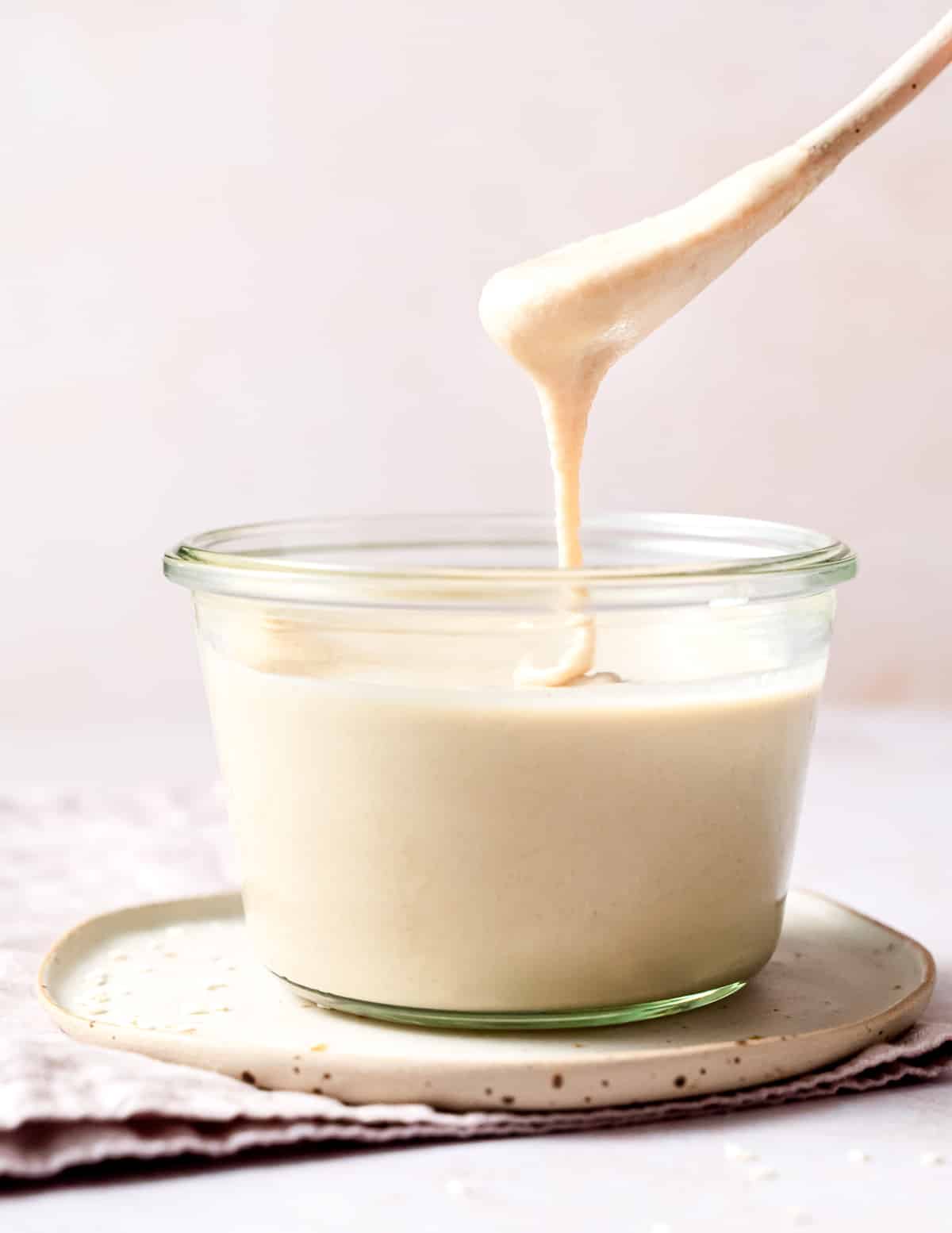a jar of tahini with a drippy spoon above