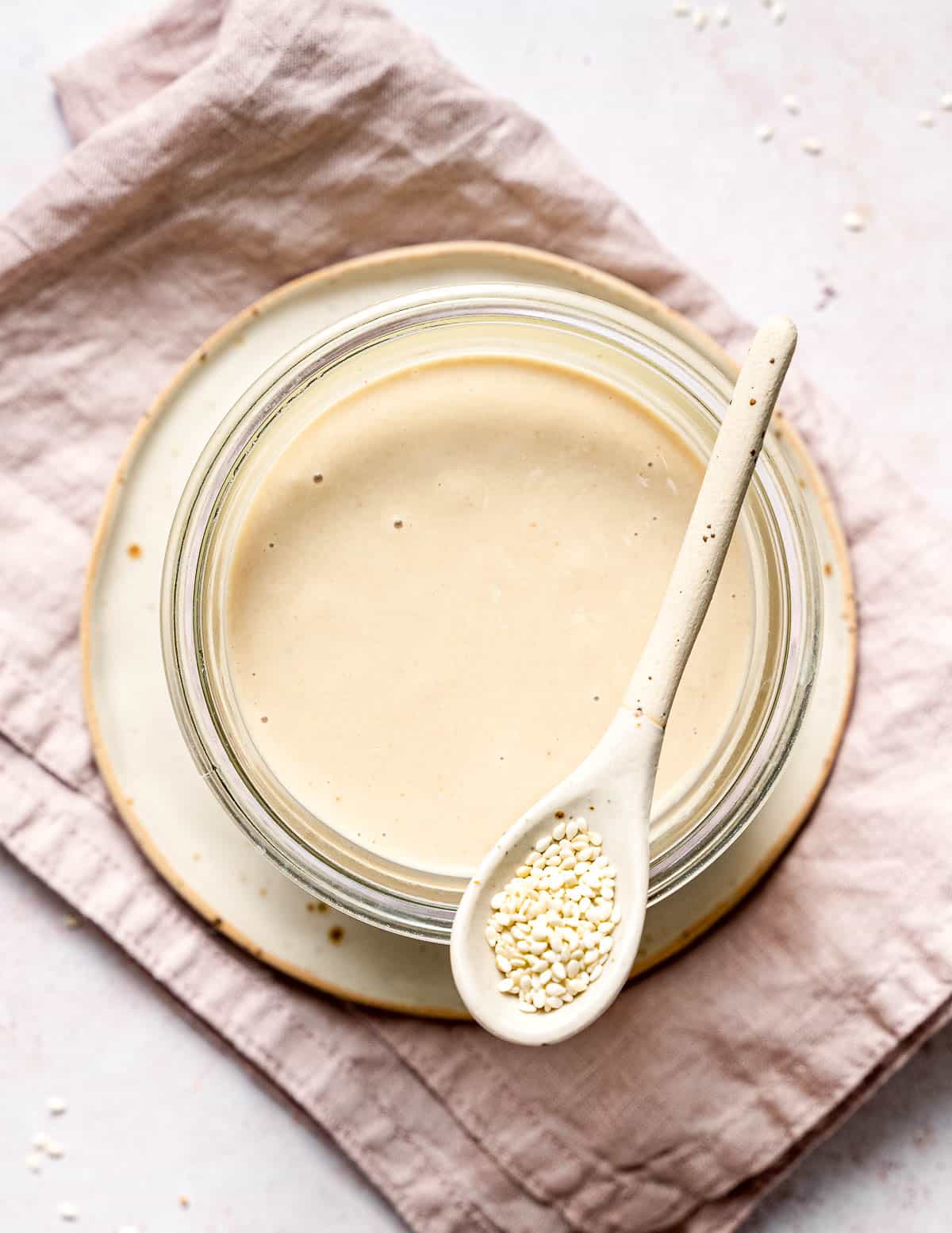 a jar of tahini with a spoon of sesame seeds resting on it taken from above