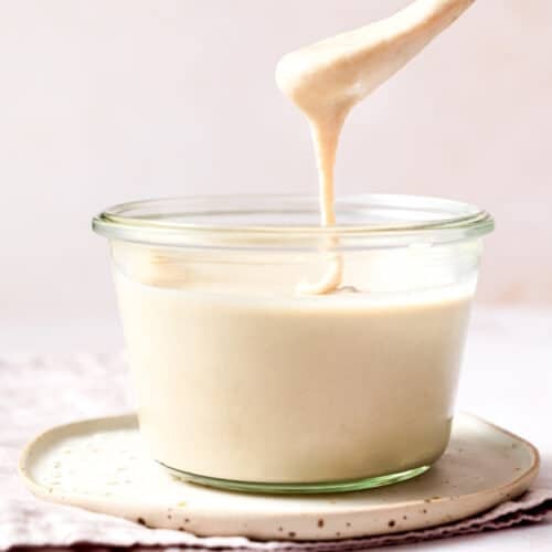 a jar of tahini with a drippy spoon above