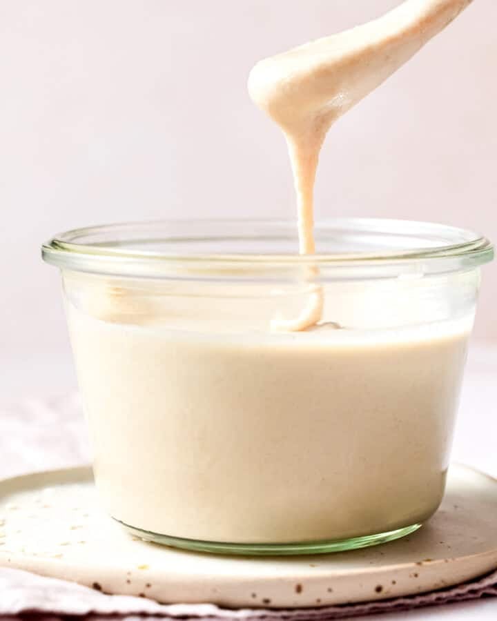 a jar of tahini with a drippy spoon above