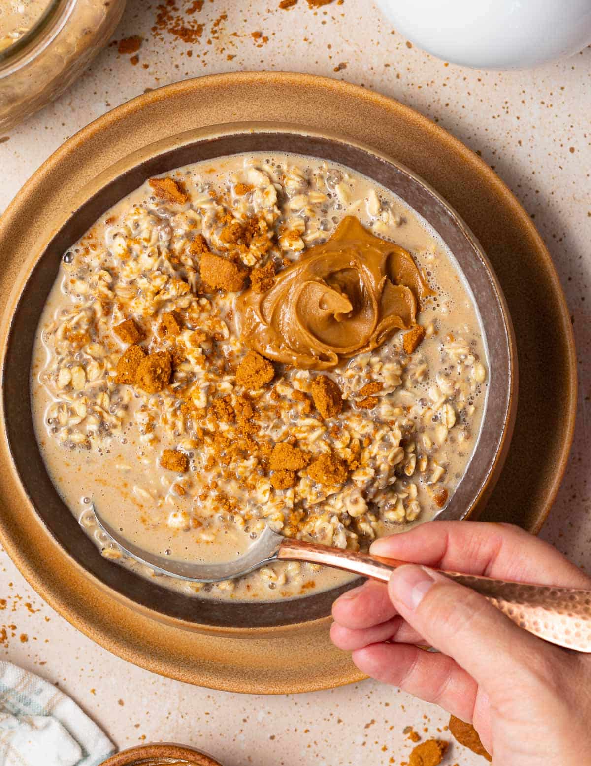 a hand holding a spoon in a bowl of Biscoff overnight oats