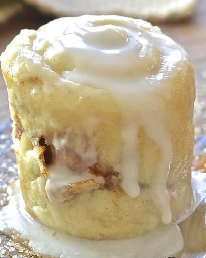 a drippy with frosting cinnamon roll in a mug turned out onto a plate.