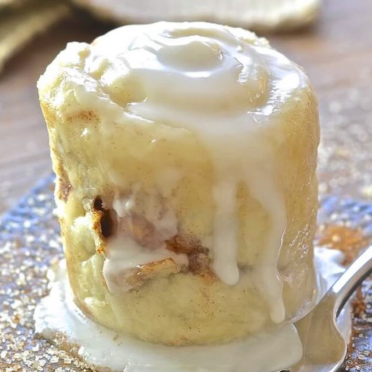 a drippy with frosting cinnamon roll in a mug turned out onto a plate.