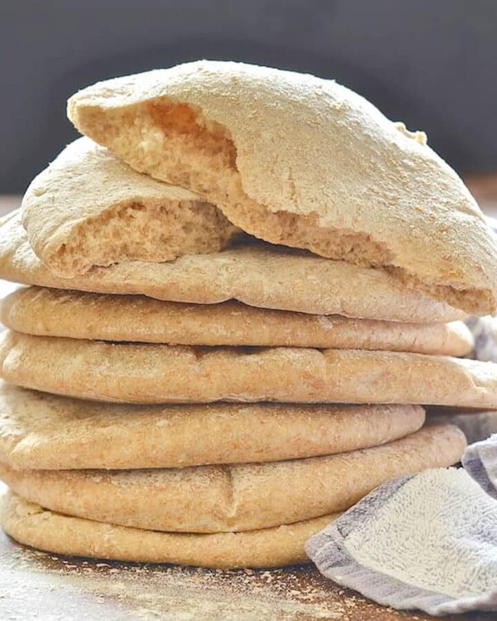 a stack of pita bread with a torn one on the top of the pile
