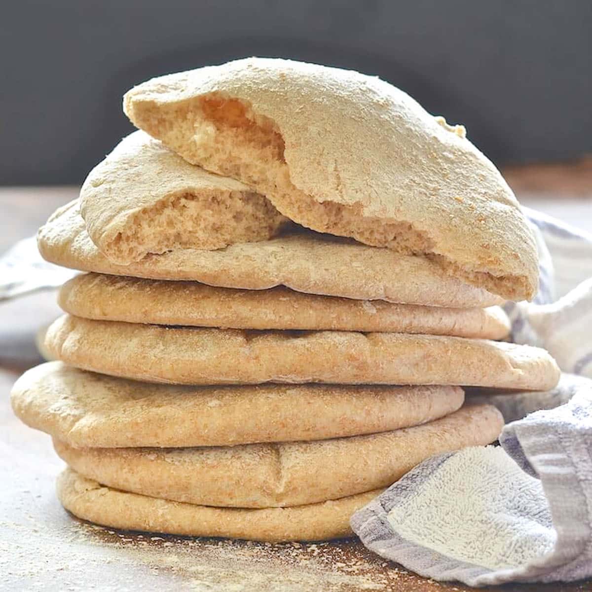 a stack of pita bread with a torn one on the top of the pile