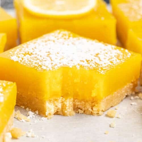 close up photo of a vegan lemon bar, sprinkled with powdered sugar and with a bite taken out of it