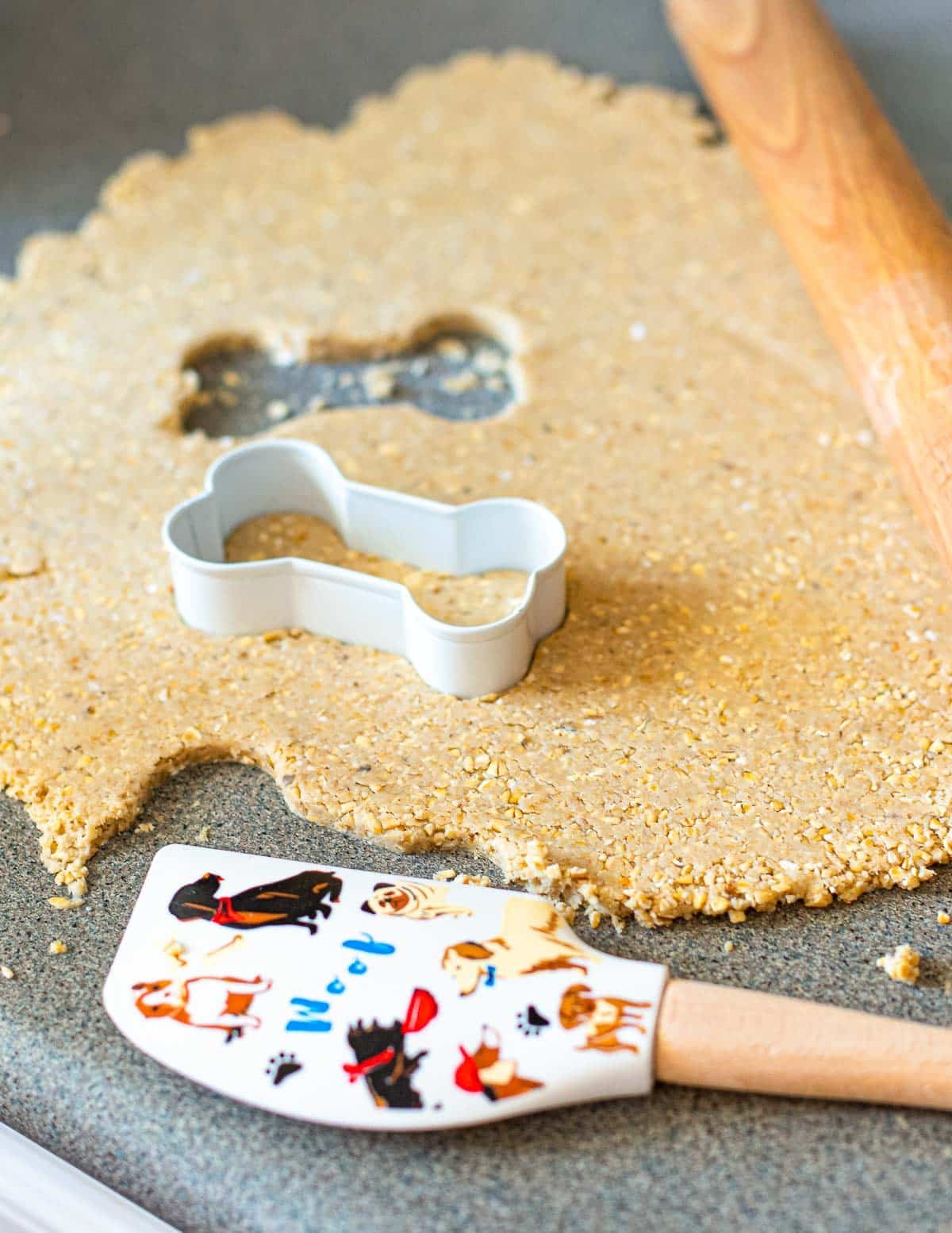 cookie dough rolled out on a counter with a bone shaped cookie cutter and woof spatula