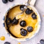 a pancake in a mug topped with blueberries, syrup and vegan butter