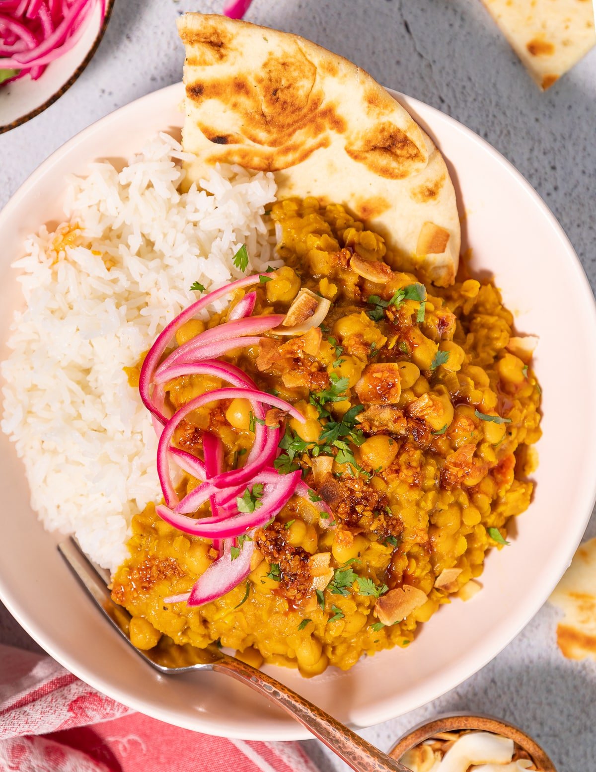a bowl of chickpea & lentil curry with rice, naan, and pickled red onions