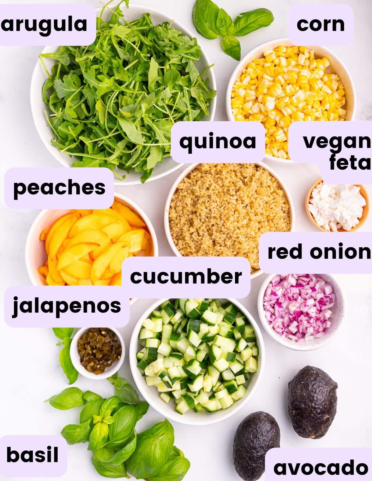 ingredients for this vegan summer salad: arugula, corn, peaches, quinoa, vegan feta, red onion, jalapenos, cucumber, avocado, basil