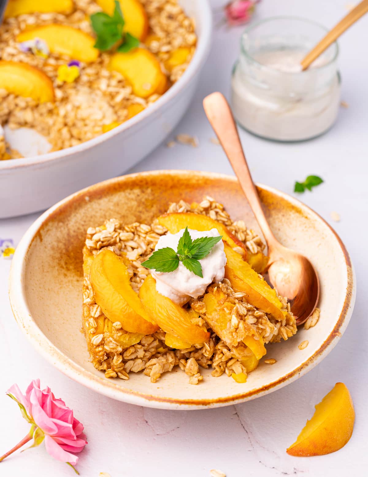 a bowl of peach baked oatmeal with a dollop of yogurt and sprig of mint