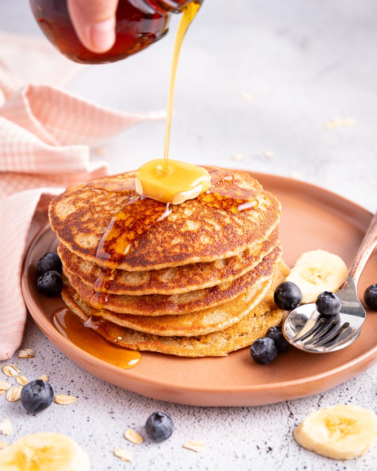 a stack of vegan banana oatmeal pancakes with a pat of vegan butter and maple syrup