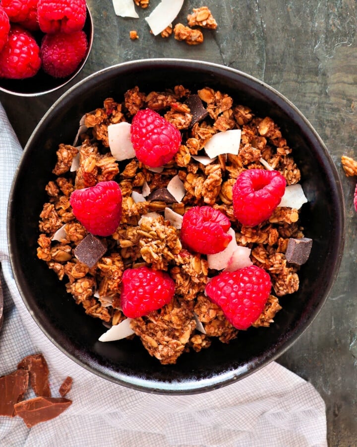 a bowl of chocolate coconut granola with fresh raspberries