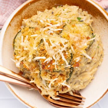 a bowl of creamy orzo with crispy, cheesy. zucchini slices on top