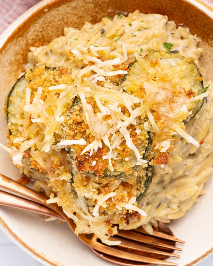 a bowl of creamy orzo with crispy, cheesy. zucchini slices on top