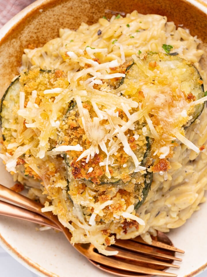 a bowl of creamy orzo with crispy, cheesy. zucchini slices on top