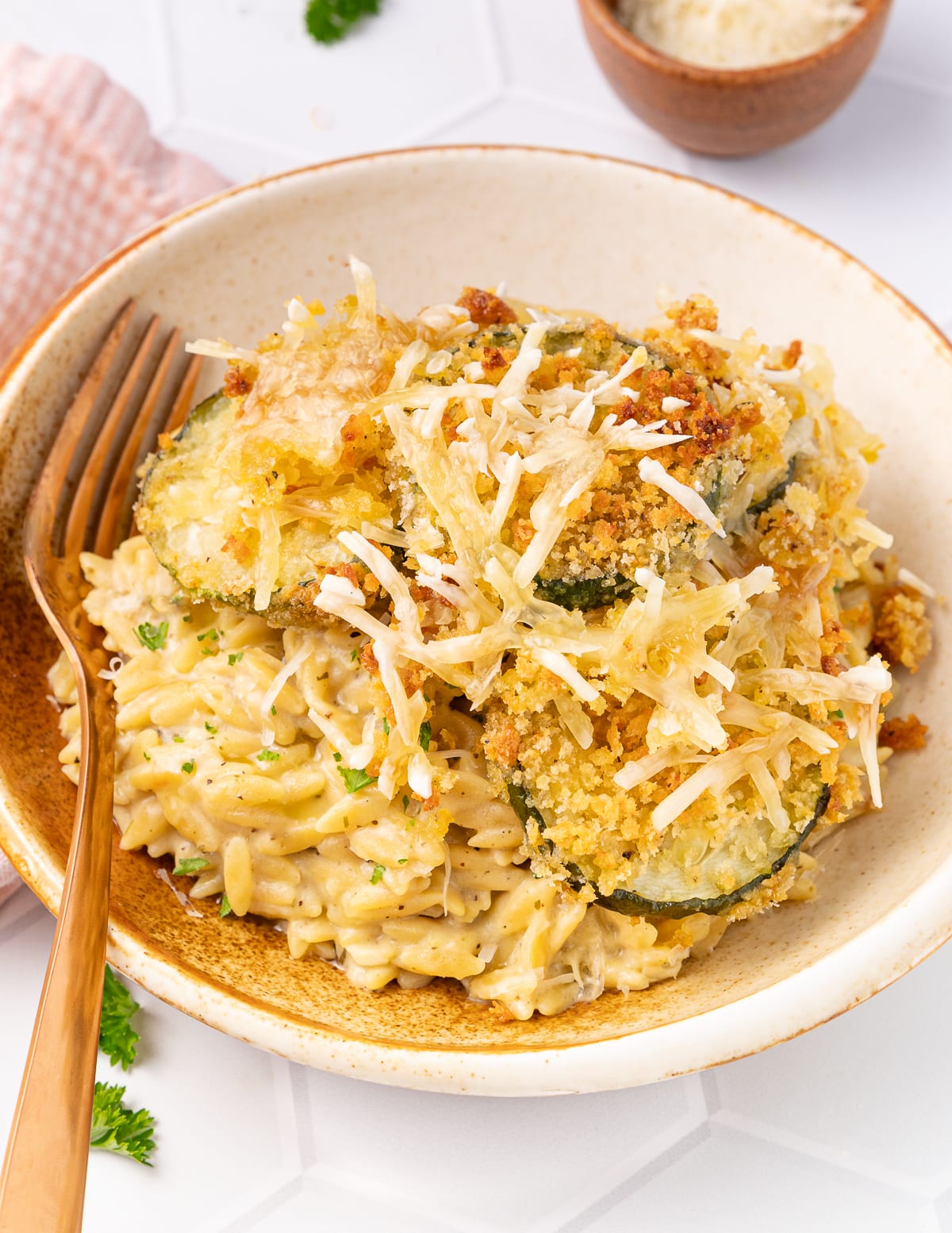 a bowl of creamy orzo with zucchini with a gold colored fork