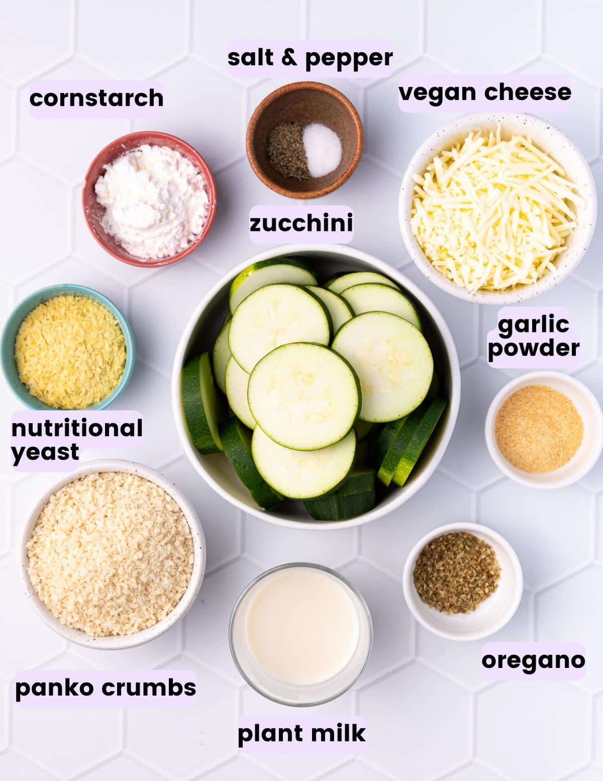 zucchini slices, cornstarch, salt, pepper, vegan cheese, garlic powder, nutritional yeast, panko crumbs, plant milk, and oregano. 